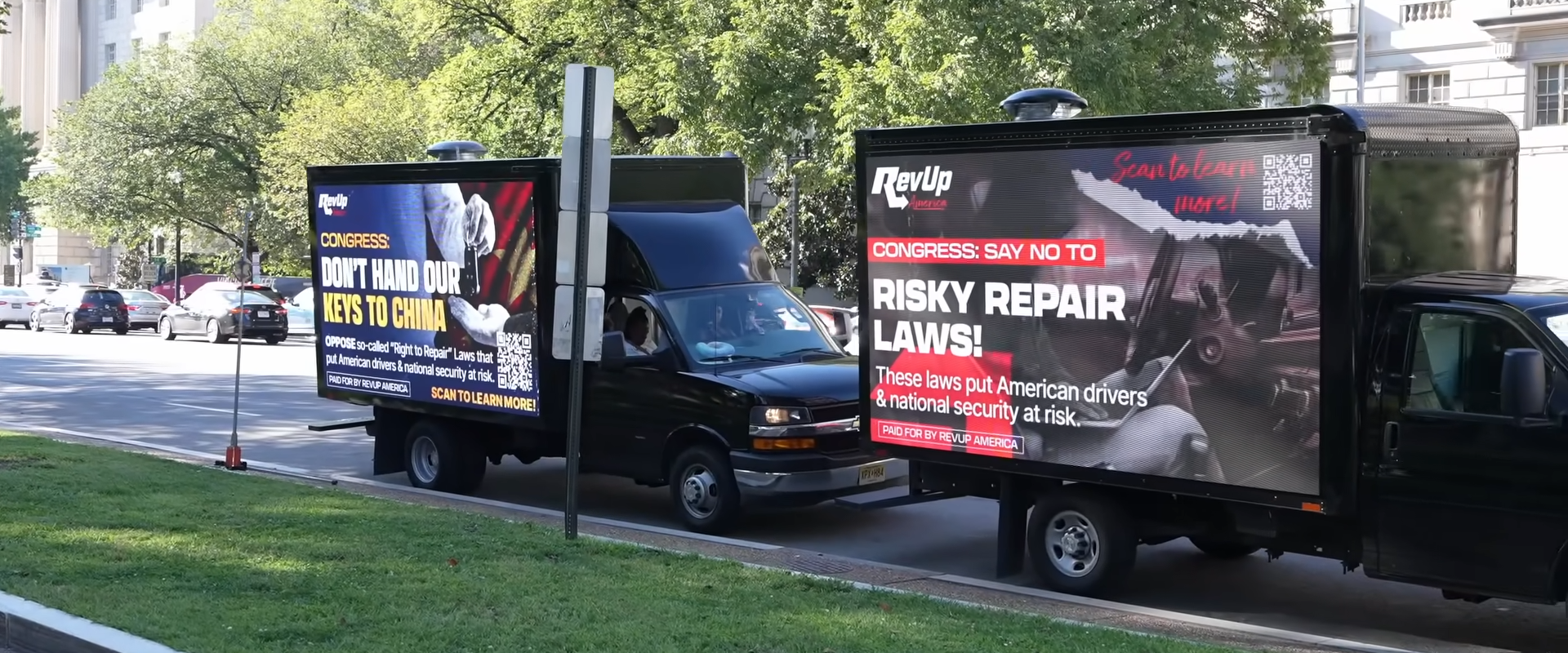 Two black mobile billboard trucks, parked one behind the other, on a road in Washington D.C. Both are sponsored by RevUp America; the one in front has a headline urging congress to "say no to risky repair laws"; the one behind has a headline "congress: don't hand our keys to china"